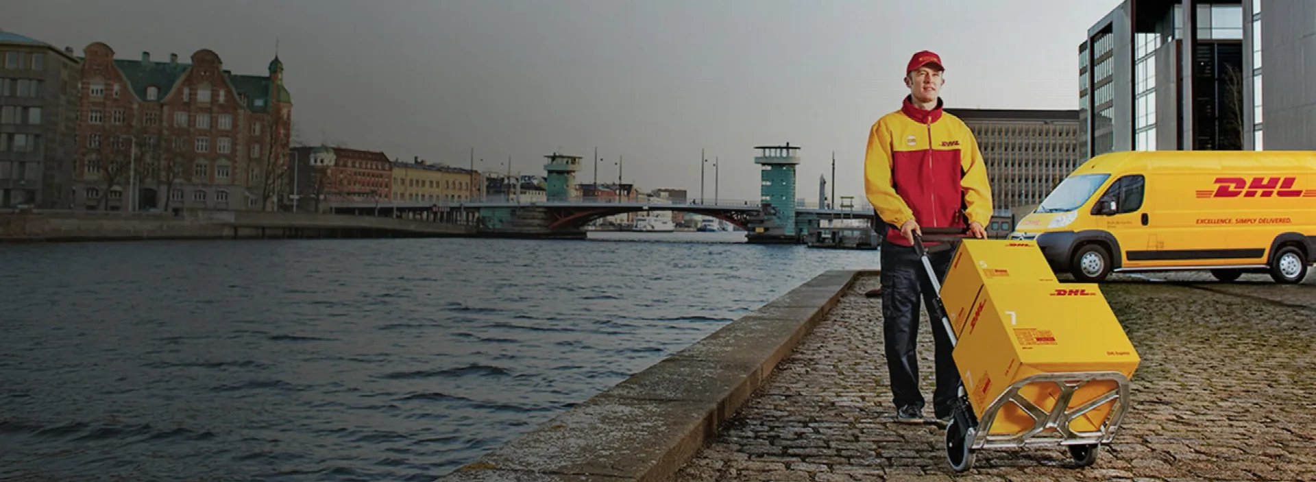 Curier DHL cu un colet și o autoutilitară pe malul unui canal
